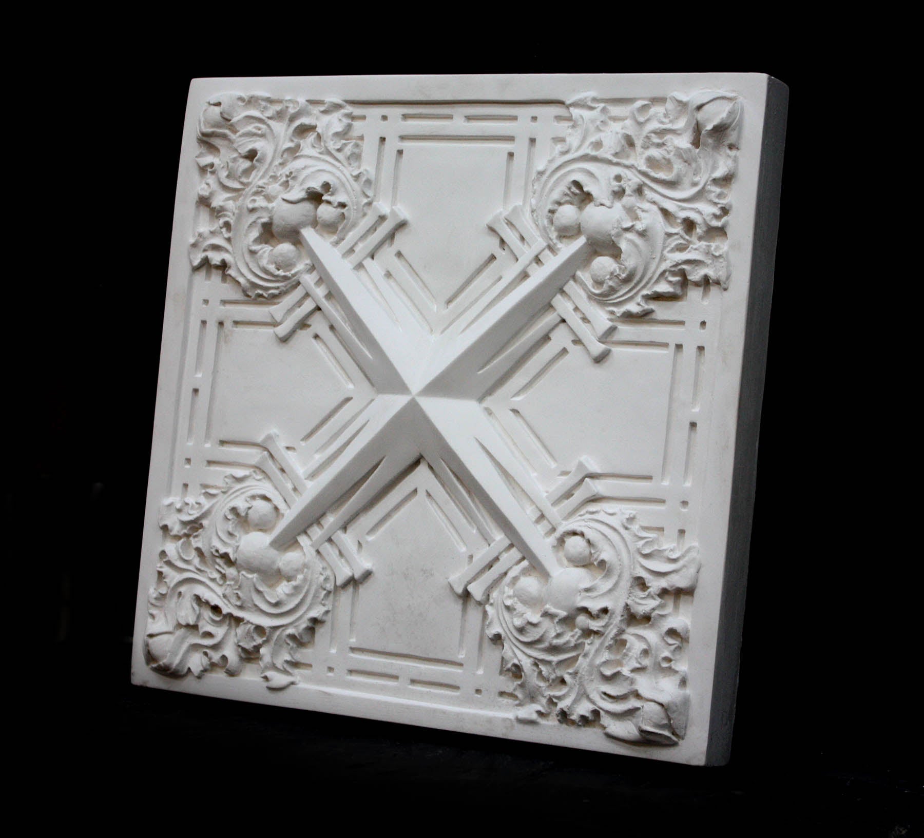 photo of white plaster cast of architectural ornament with geometric lines and leaf patterns against black background