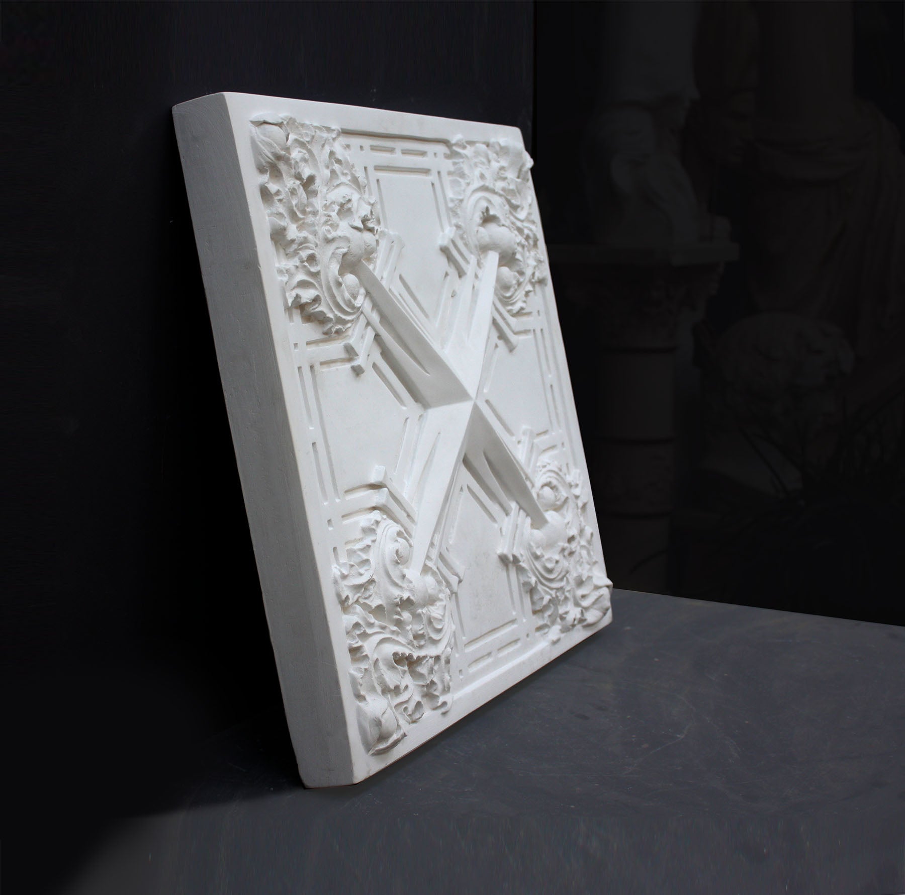 photo of white plaster cast of architectural ornament with geometric lines and leaf patterns against black background