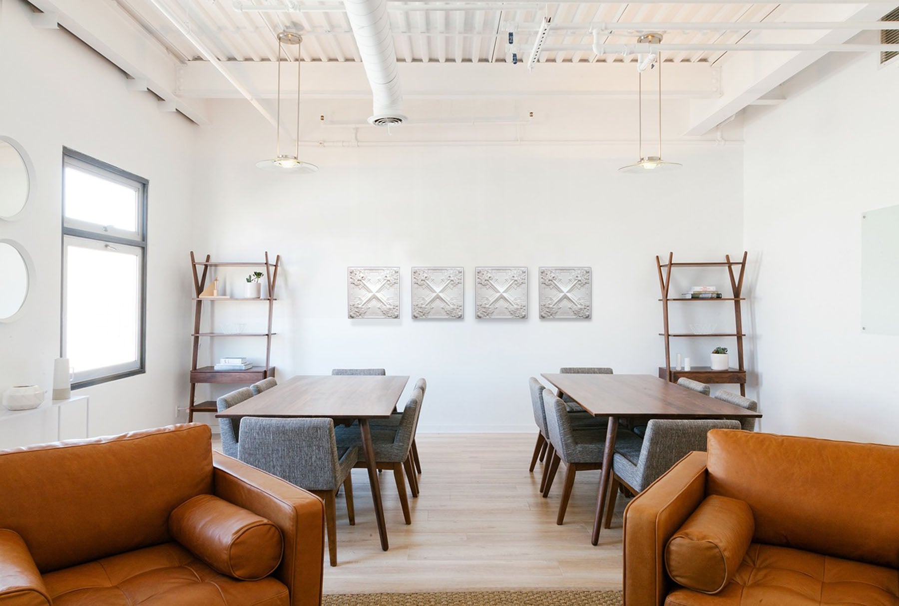 photo of white plaster casts of an architectural ornament in a row on white wall in room with two brown tables and gray chairs, and in the foreground two brown chairs