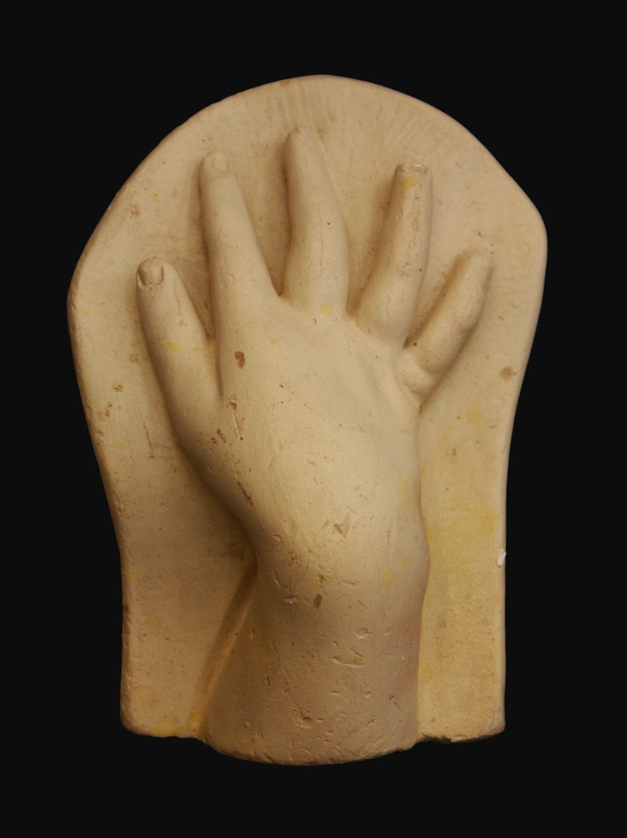 photo of off-white plaster cast sculpture of baby hand on panel against black background