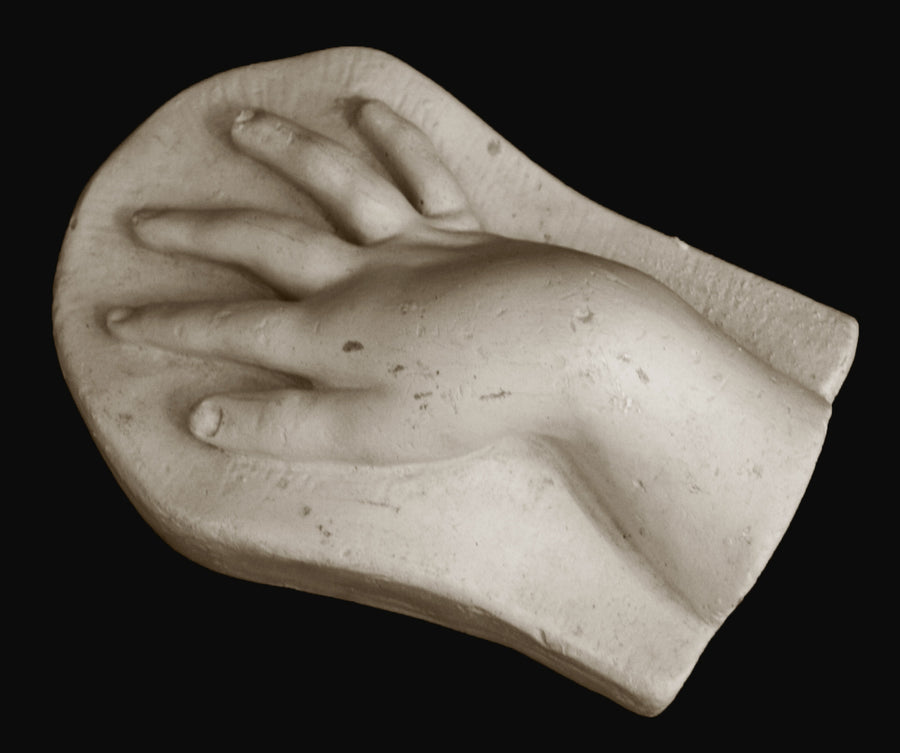 photo of off-white plaster cast sculpture of baby hand on panel against black background