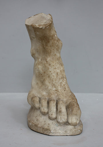 photo of yellowed plaster cast sculpture of right foot on curved surface on gray background