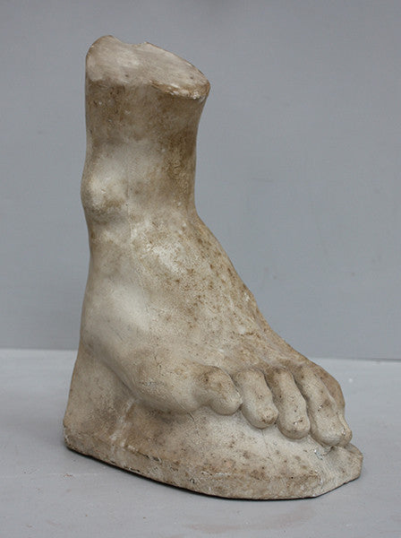 photo of yellowed plaster cast sculpture of right foot on curved surface on gray background