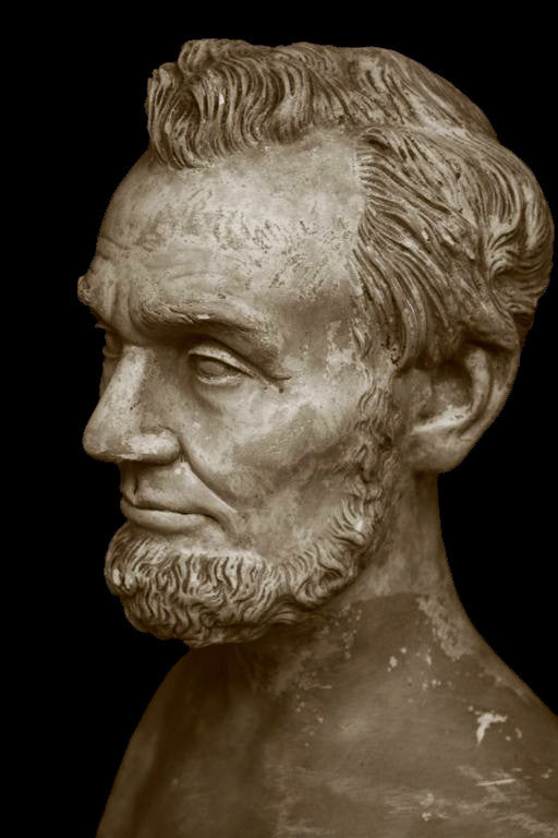photo with black background of yellowed plaster cast bust sculpture of man with beard, namely Lincoln