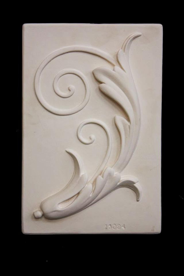 Photo of plaster cast sculpture relief of a study of a plant with scroll-like forms on a black background