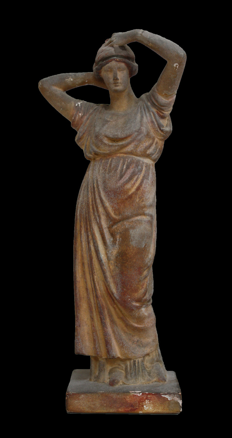 photo of plaster cast statue of a female in pink-orange tinted robes with her arms raised to her head against black background