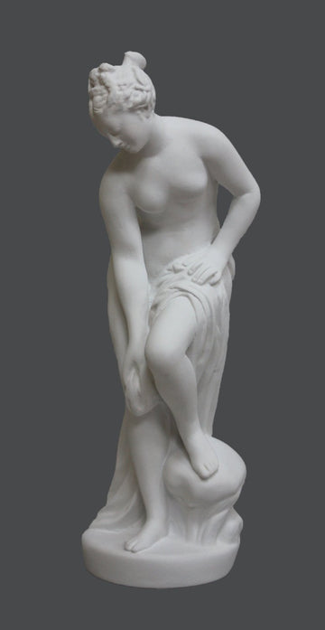photo of plaster cast of sculpture of partially nude female, namely Venus, leaning forward to wash her left leg with a gray background