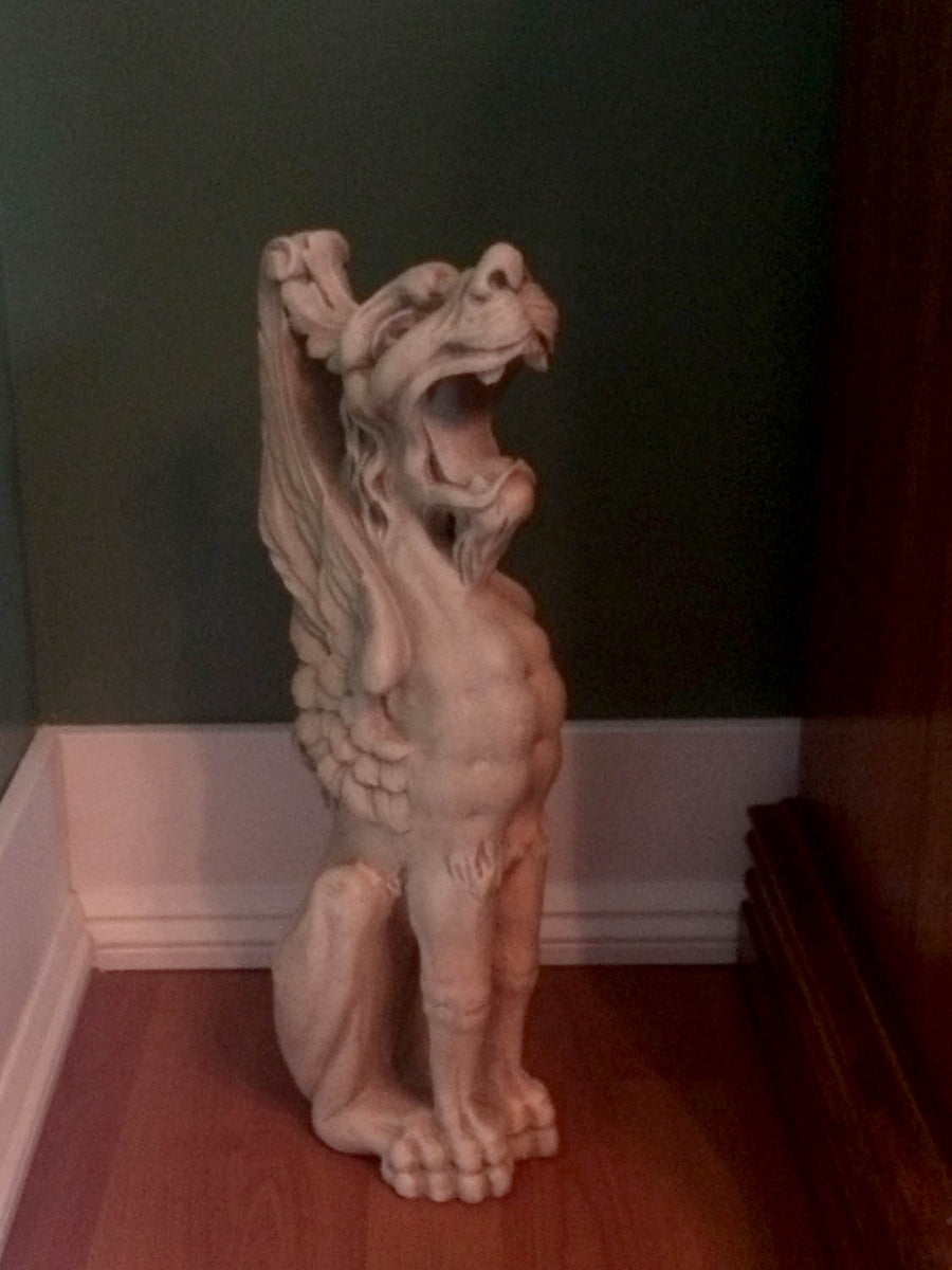 hoto of plaster cast sculpture of imaginary seated winged lion in front of a green wall with white baseboard