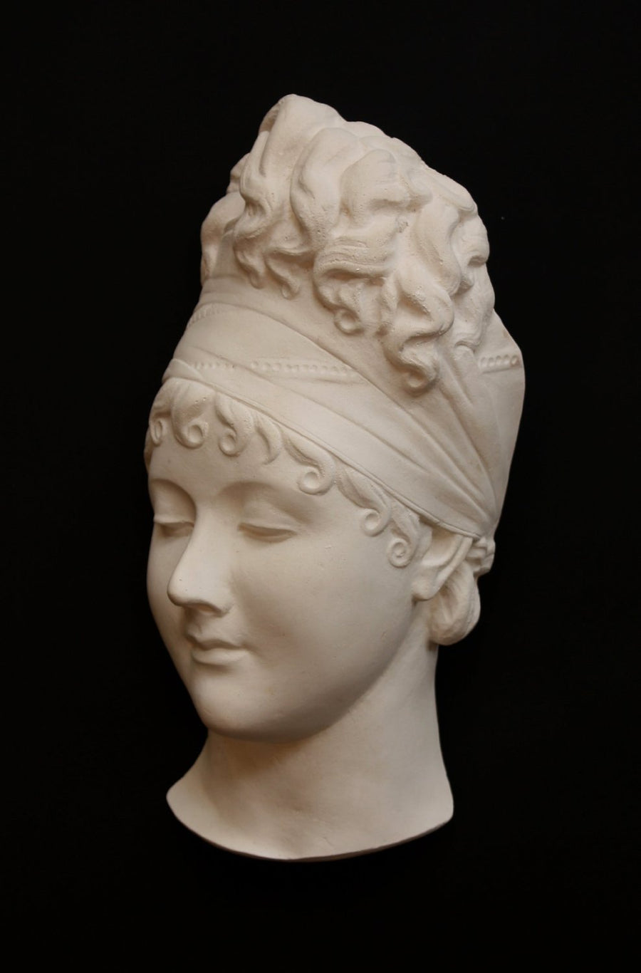 photo with black background of plaster cast sculpture of face of Madame Recamier with high up-do and ribbon over forehead